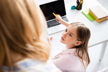 Overhead view of kid looking at mother while pointing at laptop during online educationの写真素材
