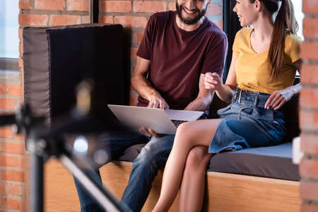 selective focus of happy businesswoman and bearded businessman sitting on window bench with laptop
