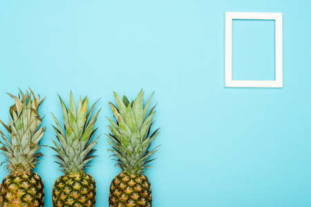 top view of ripe pineapples near square empty frame on blue backgroundの写真素材
