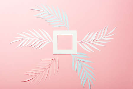 top view of white, pink and blue paper cut palm leaves and square frame on pink background