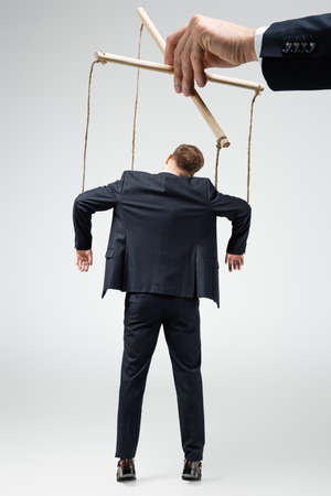 cropped view of puppeteer holding businessman marionette on strings isolated on grayの写真素材
