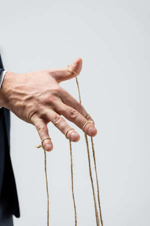 partial view of puppeteer with strings on fingers isolated on gray
