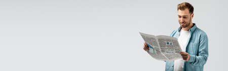 smiling young man reading newspaper isolated on gray, panoramic shotの写真素材
