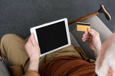cropped view of senior man holding digital tablet with blank screen and credit card, overhead view