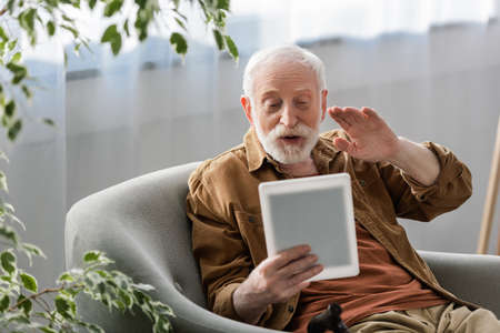 selective focus of happy senior man waving hand during video call on digital tablet