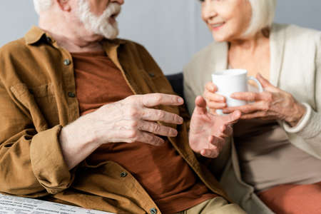 selective focus of senior man gesturing while talking to smiling wife holding cup of teaの写真素材