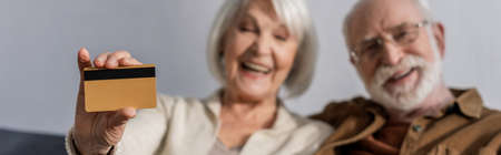 selective focus of cheerful senior woman showing credit card near smiling man, website headerの写真素材