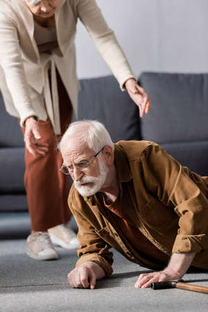 cropped view of woman helping fallen senior husband to get up from floorの写真素材