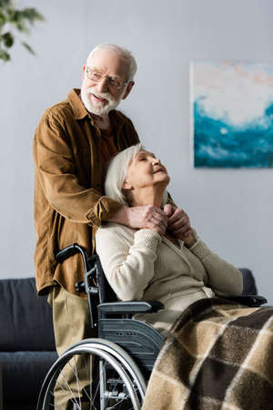 smiling senior man holding hand of handicapped wife sitting in wheelchairの写真素材