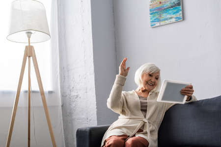 excited senior woman sitting with raised hand while using digital tabletの写真素材