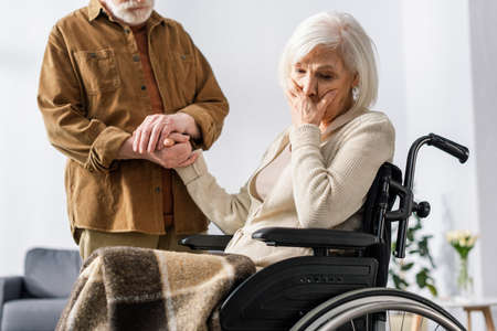 cropped view of man holding hand of disabled wife, sick on dementia, holding hand on face while...