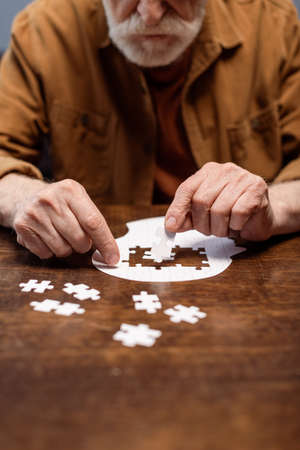 cropped view of senior man playing jigsaw puzzle for dementia rehabilitationの写真素材