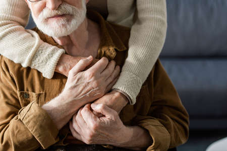 cropped view of woman embracing senior husband and holding his handsの写真素材