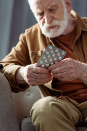 selective focus of lonely senior man feeling bad and holding pillsの写真素材