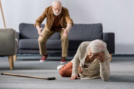 selective focus of senior man hurrying to help wife lying on floor near walking stickの写真素材