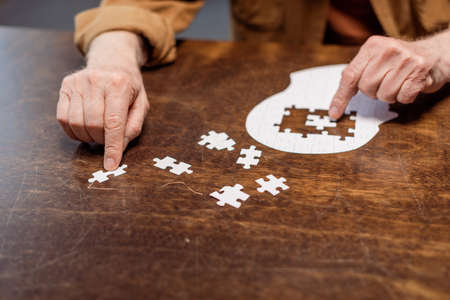 partial view of senior man playing jigsaw puzzle as dementia therapyの写真素材
