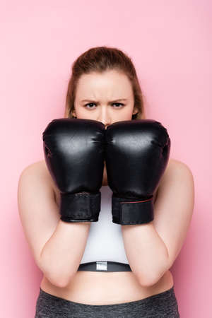 serious overweight girl obscuring face with boxing gloves while looking at camera on pinkの写真素材