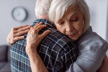 senior woman with closed eyes embracing husband sick on dementiaの写真素材