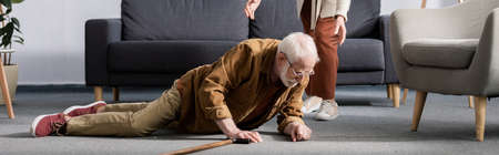 partial view of woman helping fallen senior husband to get up from floor, horizontal conceptの写真素材