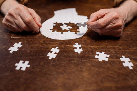 cropped view of ill senior man collecting jigsaw puzzle for dementia therapyの写真素材