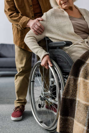 cropped view of senior man touching arm of handicapped, diseased wife in wheelchairの写真素材
