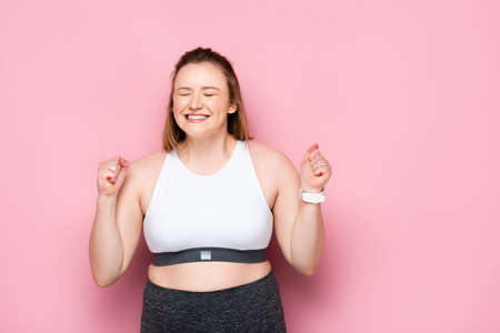 excited overweight girl showing winner gesture on pinkの写真素材