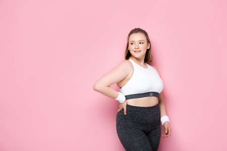 pretty, smiling overweight girl standing with hand on hip on pinkの写真素材