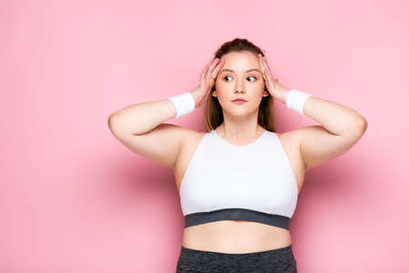 shocked overweight girl touching head and looking away on pinkの写真素材