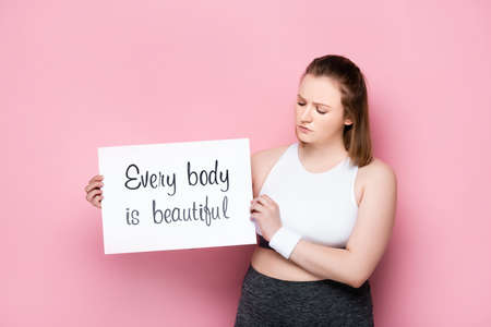 serious overweight holding placard with every body is beautiful inscription on pinkの写真素材