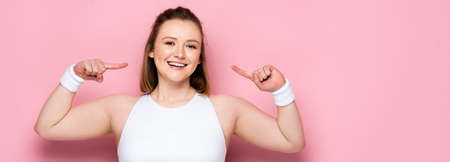 panoramic crop of cheerful overweight girl pointing with fingers at herself on pink