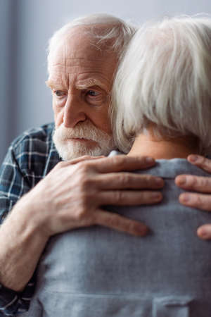 senior man, suffering from dementia, hugging wife and looking awayの写真素材