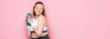 horizontal image of pretty overweight girl holding sports bottle and smiling with closed eyes on...