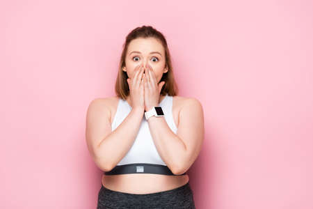 shocked overweight girl covering mouth with hands on pinkの写真素材