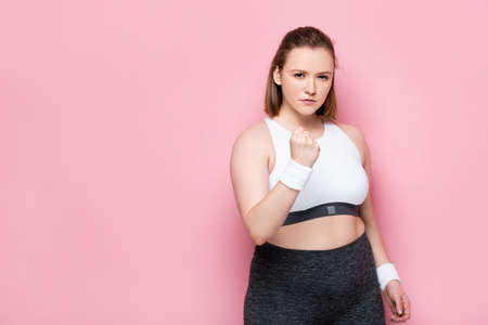 angry overweight girl showing clenched fist and looking at camera on pinkの写真素材