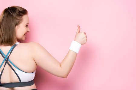 back view of overweight girl showing thumb up on pink