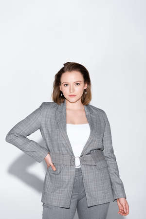 elegant, confident overweight girl looking at camera while posing with hand on hip on gray