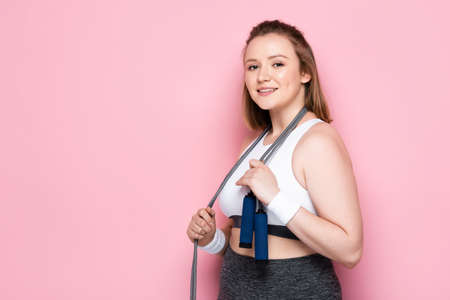 pretty overweight girl with jumping rope around neck smiling at camera on pink