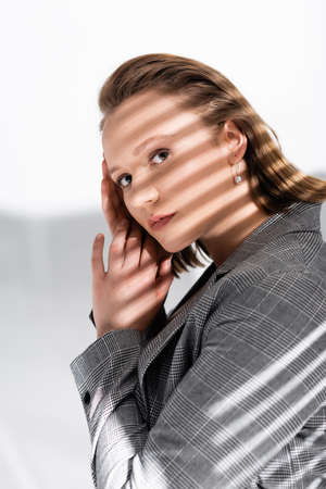 beautiful overweight girl holding hands near face while looking at camera on white in sunlight with...