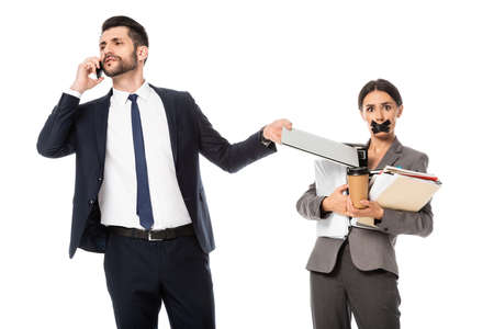 bearded businessman talking on smartphone near secretary with duct tape on mouth isolated on white