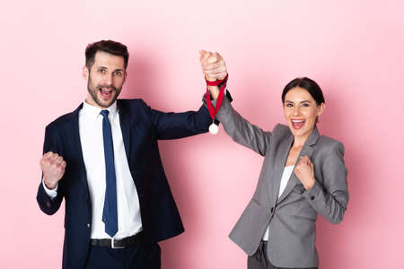excited businessman and businesswoman holding golden medal and gesturing on pink, gender equality conceptの写真素材