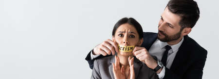 horizontal image of businessman touching duct tape with sexism lettering on mouth of scared...