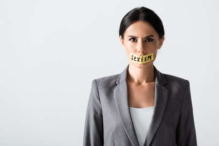Businesswoman with sexism lettering on duct tape looking at camera isolated on white