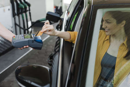 Selective focus of worker of gas station holding payment terminal near smiling woman paying with credit card in carの写真素材