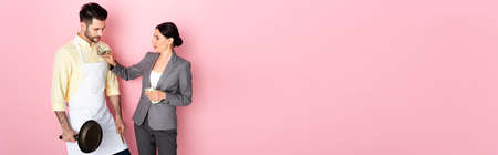 website header of businesswoman putting money in pocket of handsome man in apron holding frying pan on pinkの写真素材