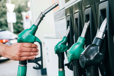 Cropped view of man holding fueling nozzle on gas station on urban street