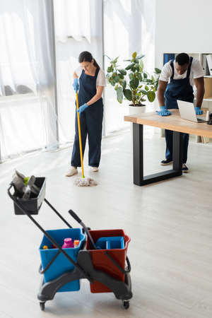 Selective focus of multiethnic cleaners washing floor and table while working in office