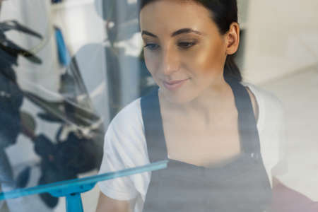 Selective focus of attractive cleaner using squeegee handle while cleaning glass of window in office