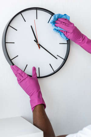 Cropped view of african american cleaner cleaning clock on wall in officeの写真素材