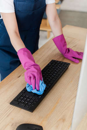Cropped view of worker of cleaning service cleaning computer keyboard with rag on table