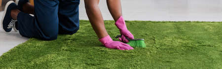 Panoramic crop of african american worker of carpet cleaning service using brush in living roomの写真素材
